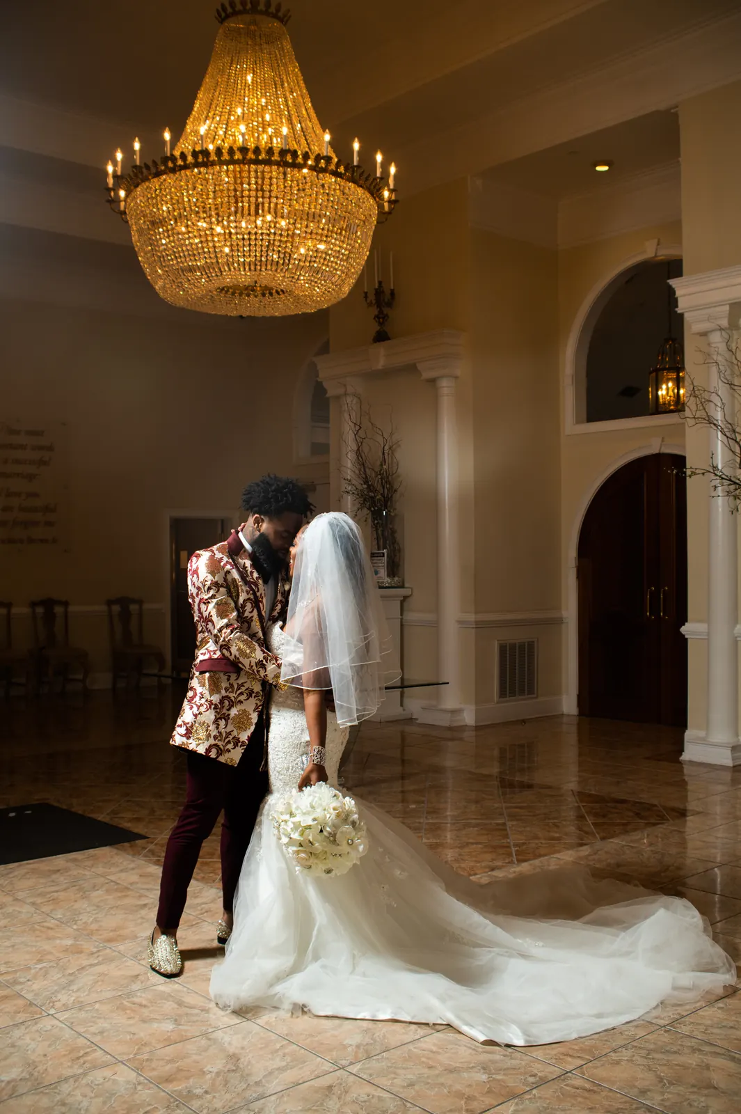 Bride and groom dancing beneath a crystal chandelier in a mansion foyer