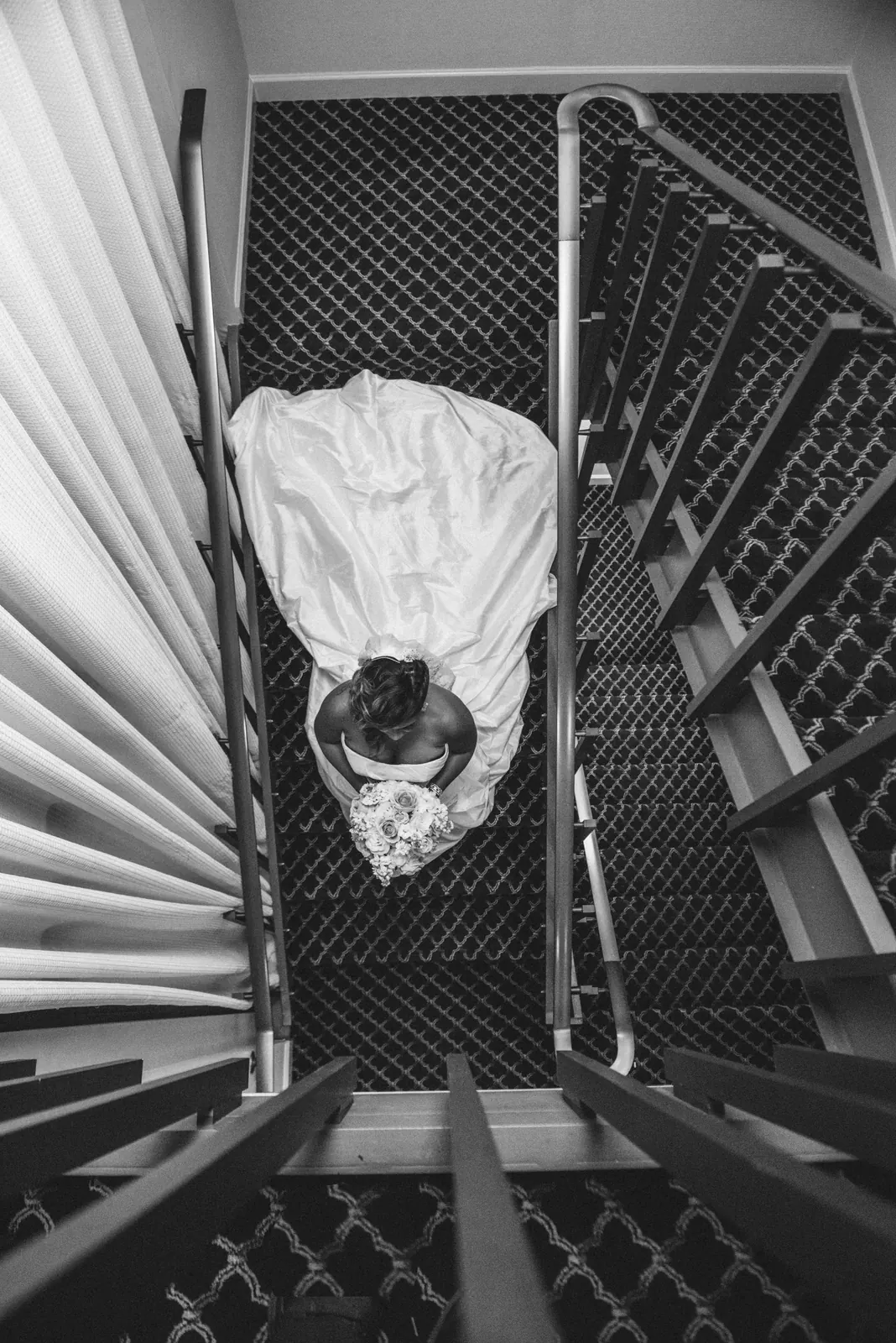 Black and white overhead photograph of a wedding dress laid over a spiral staircase