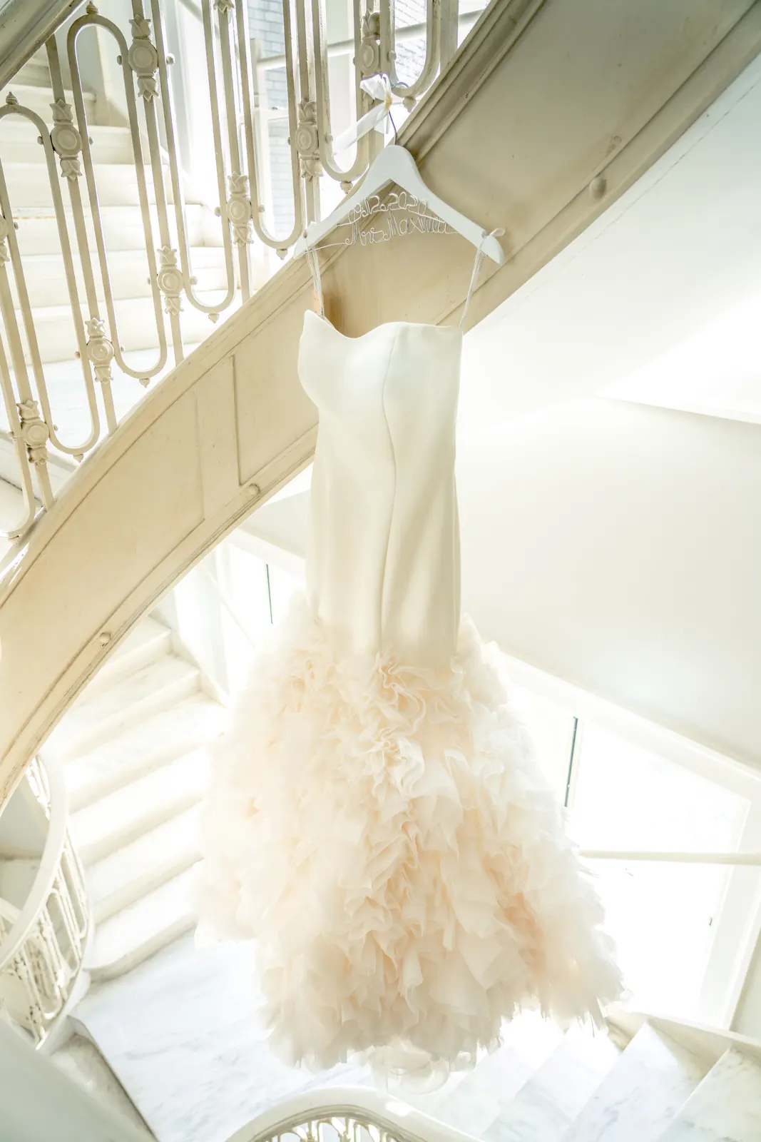 Wedding dress hanging in a bright window with feathered skirt detail