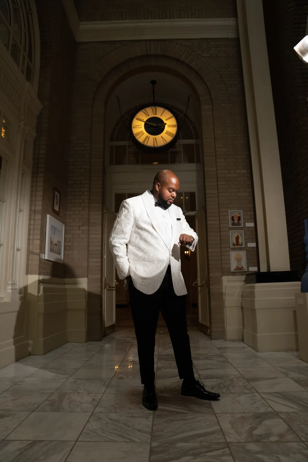 Groom in a white tuxedo jacket fastening his cufflink in an ornate marble hallway
