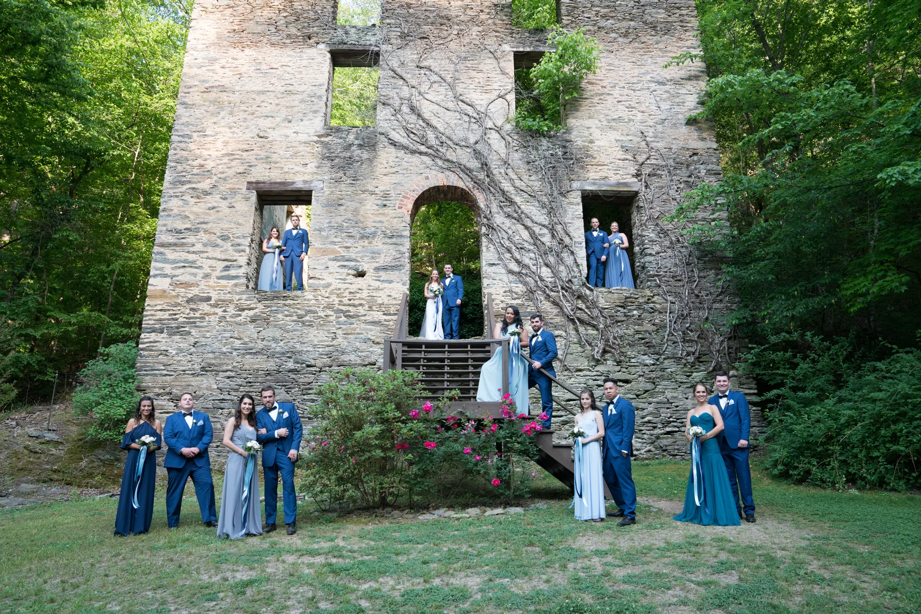 Full wedding party posed across the stone ruins and tower of an old mill, bride and groom on the staircase